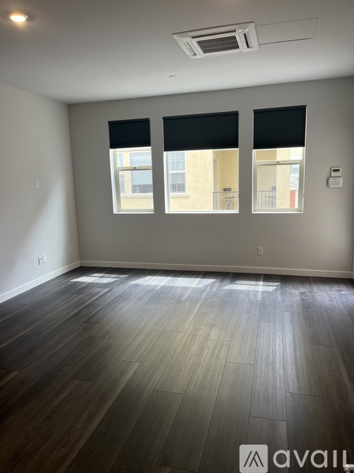 A room with wooden flooring and two windows with blinds.