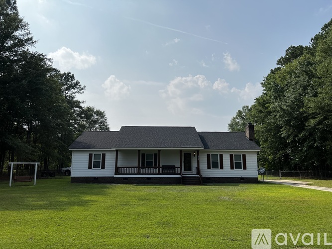 A white house with a grey roof and a porch surrounded by trees.