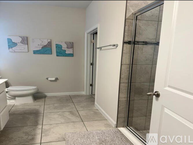 A bathroom with a toilet, a glass shower door, and three pictures on the wall.