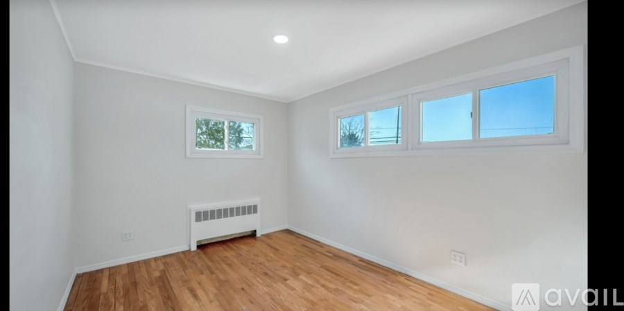 A room with wooden floors and white walls, with a window and a radiator.