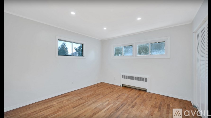 A room with wooden flooring and two windows.