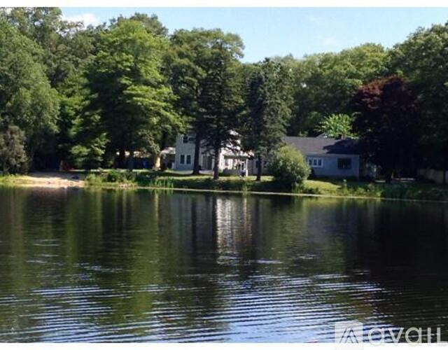 A serene lake surrounded by lush green trees and a white house in the distance.