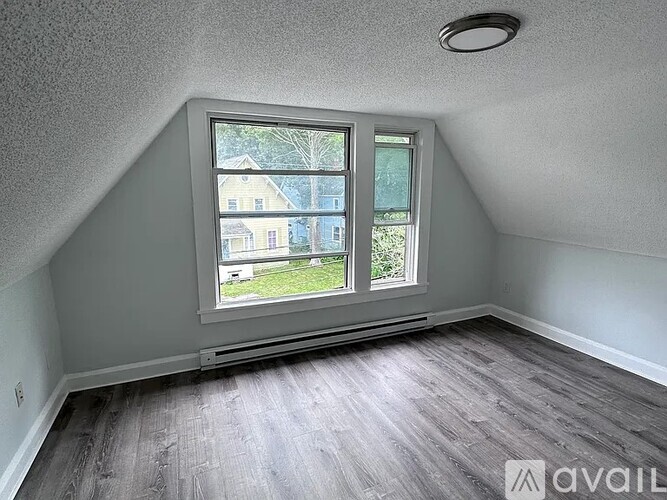 A room with a large window and wooden flooring is available for rent.