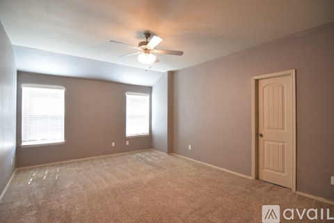 A room with a carpeted floor, a ceiling fan, and a door.