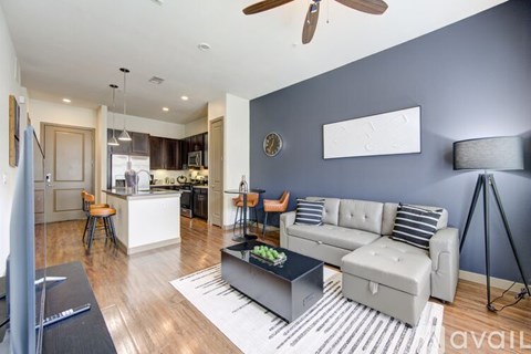 A modern living room with a grey sofa and a kitchen in the background.