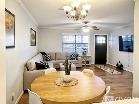 A living room with a wooden table and chairs, a couch, a ceiling fan, and a painting on the wall.