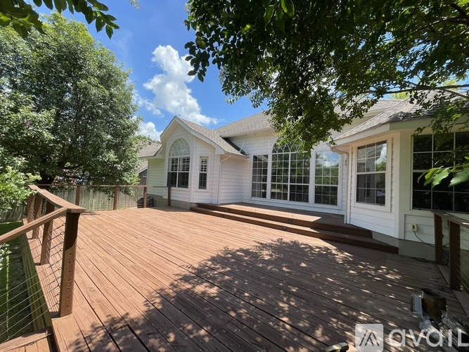 A wooden deck leads to a white house with a glass door and windows.