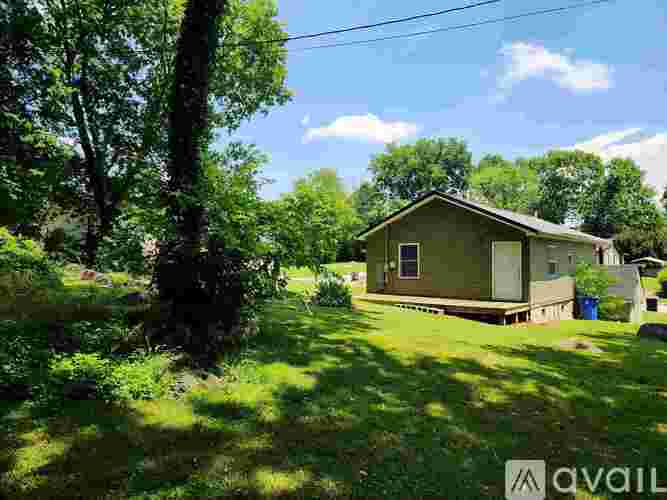 A house is surrounded by greenery and has a blue trash bin outside.