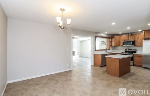 A well-lit, spacious kitchen and living area with wooden cabinets and a tiled floor.