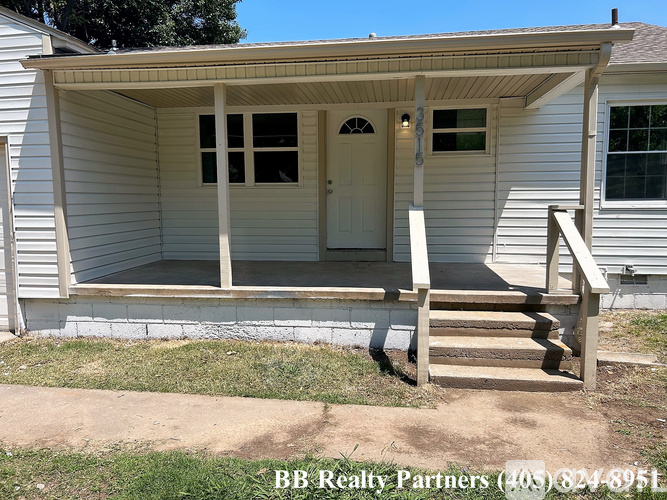 A white house with a porch and a BB Realty Partners sign.