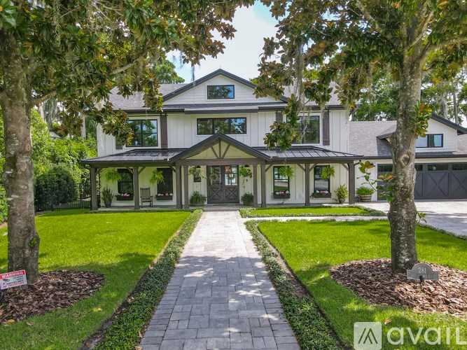 A house with a white exterior and a grey roof is surrounded by trees and has a walkway leading to the front door.