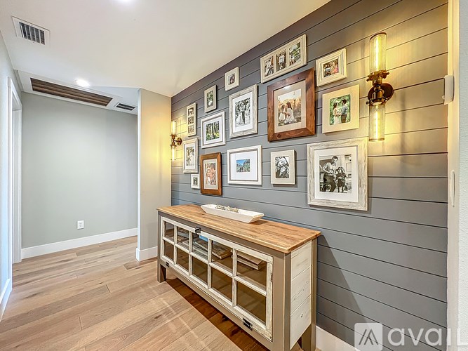 A wall of framed pictures is on a wall above a wooden table.