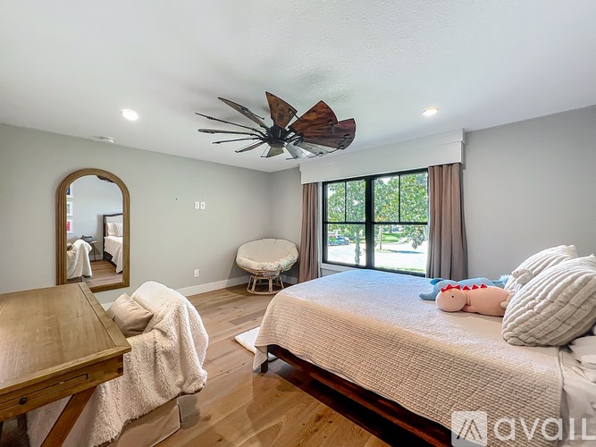 A bedroom with a bed, a table, a mirror, and a window with a view of trees.