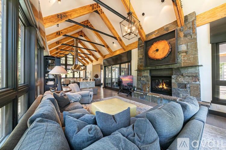 A large grey couch sits in the middle of a spacious room with a stone fireplace and wooden beams.