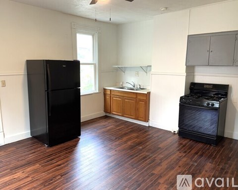 A black refrigerator stands in a kitchen with wood floors and white walls.
