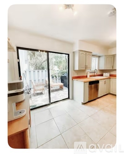 A kitchen with a white tile floor and a view of a backyard through the sliding glass doors.