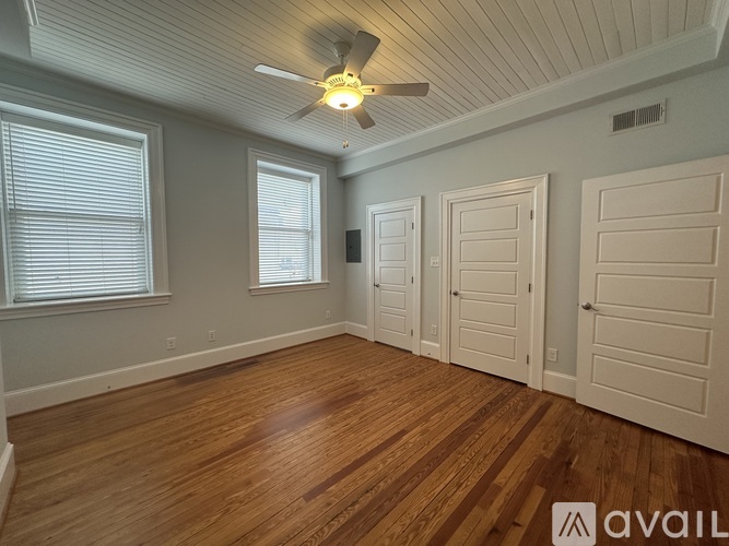 A room with wooden floors and white walls has a ceiling fan and three doors.