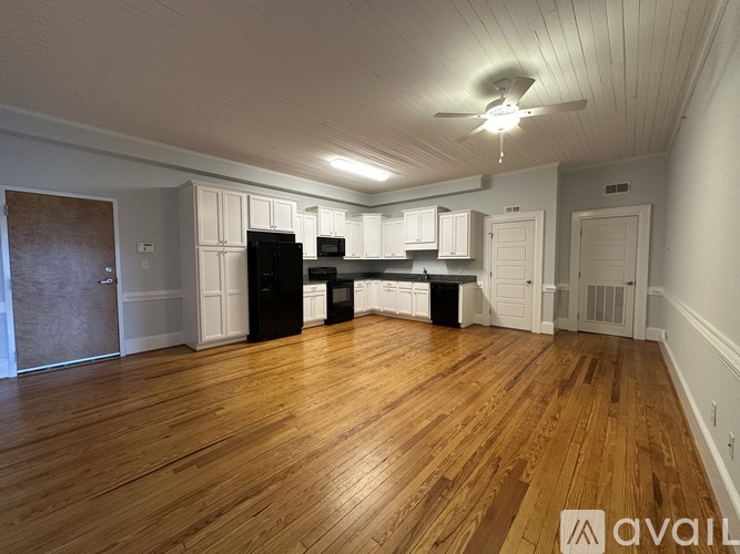 A spacious room with wooden floors and a kitchen area with white cabinets.