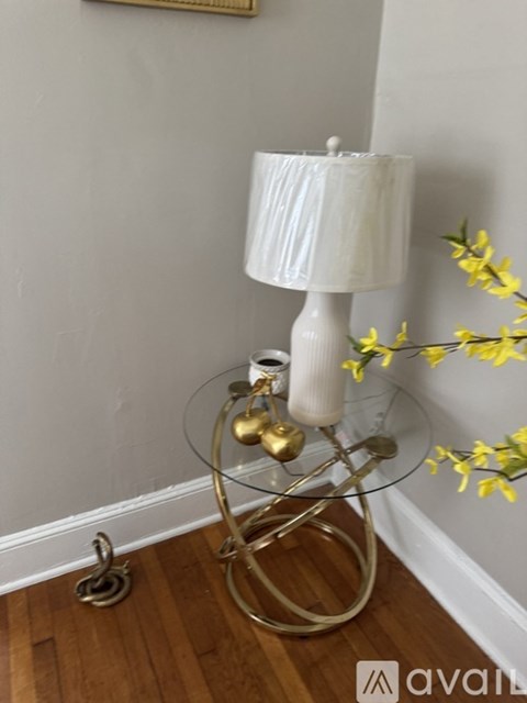 A white lamp with a gold base and a glass table stand on a wooden floor.