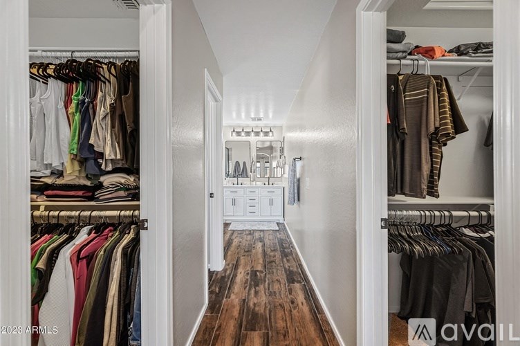 A walk-in closet with clothes hanging on racks and a wooden floor.