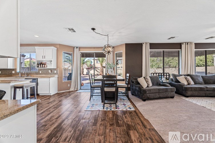 A living room with a brown floor and a dining area with a table and chairs.