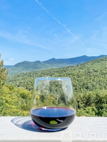 A glass of red wine is on a table with a mountainous landscape in the background.