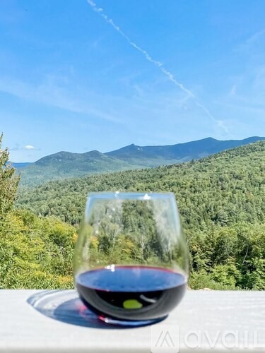 A glass of red wine is on a table with a mountainous landscape in the background.