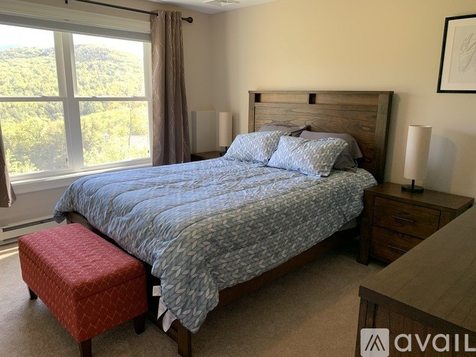 A bedroom with a large bed and a window overlooking a green landscape.