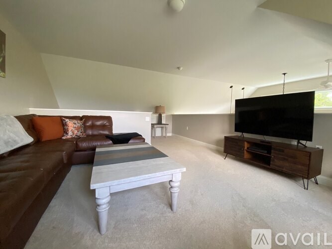 A living room with a brown leather couch, a grey coffee table, and a black television.