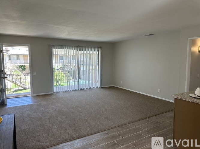A spacious room with a carpeted floor, a window with blinds, and a door leading to a balcony.