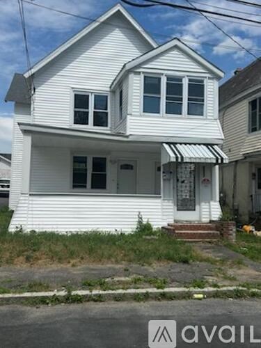 A white house with a striped awning is for sale.