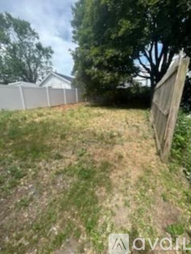 A grassy area with a fence and a tree in the background.
