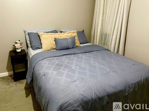 A bed with a grey comforter and blue pillows is in a room with a carpeted floor.