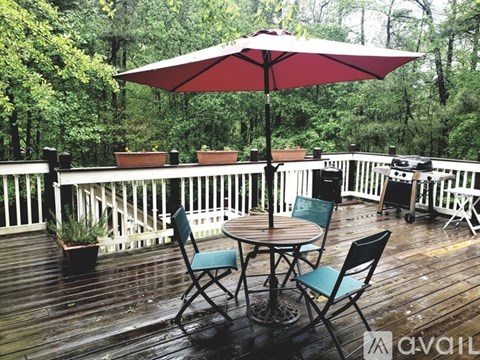 A red umbrella is on a wooden deck with a table and chairs.