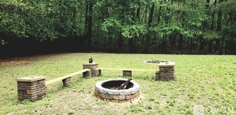 A fire pit is surrounded by a brick wall and a wooden fence in a grassy area.