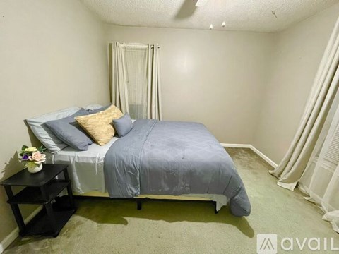 A bedroom with a bed, nightstand, and window with curtains.