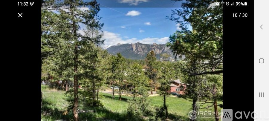A mountain range is visible through a foreground of trees and a house.