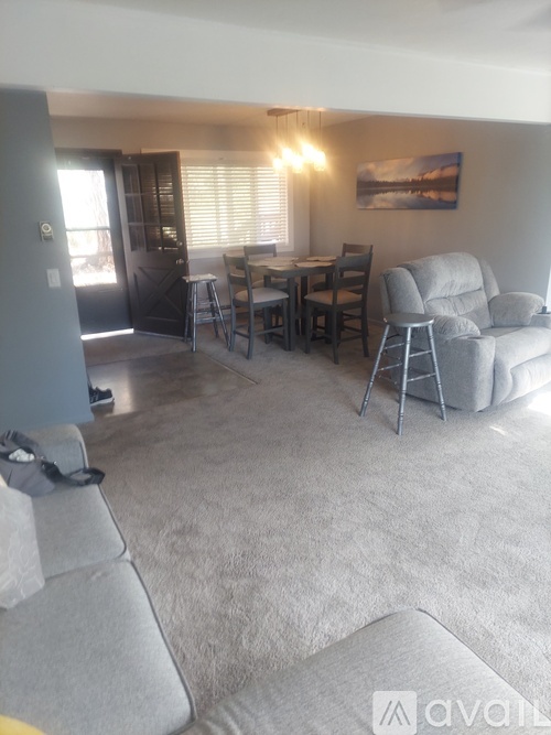 A living room with a grey couch, a dining table with chairs, and a painting on the wall.
