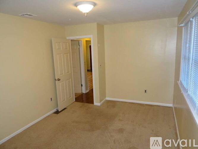 A room with beige walls and carpeting, a white door, and a window with blinds.