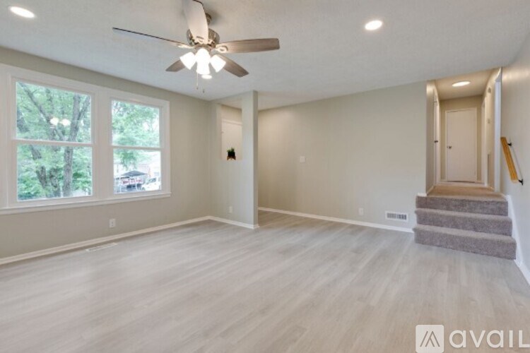 A spacious room with a ceiling fan and light, large windows, and a staircase leading to another room.