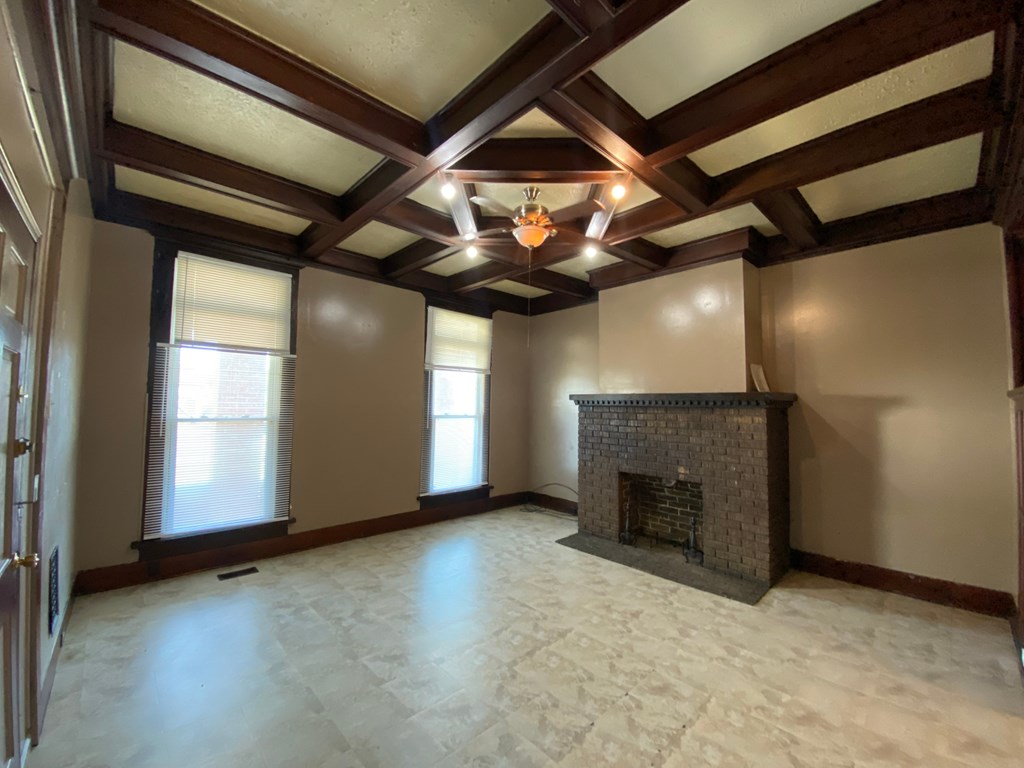 A large, empty room with a fireplace and wooden beams on the ceiling.
