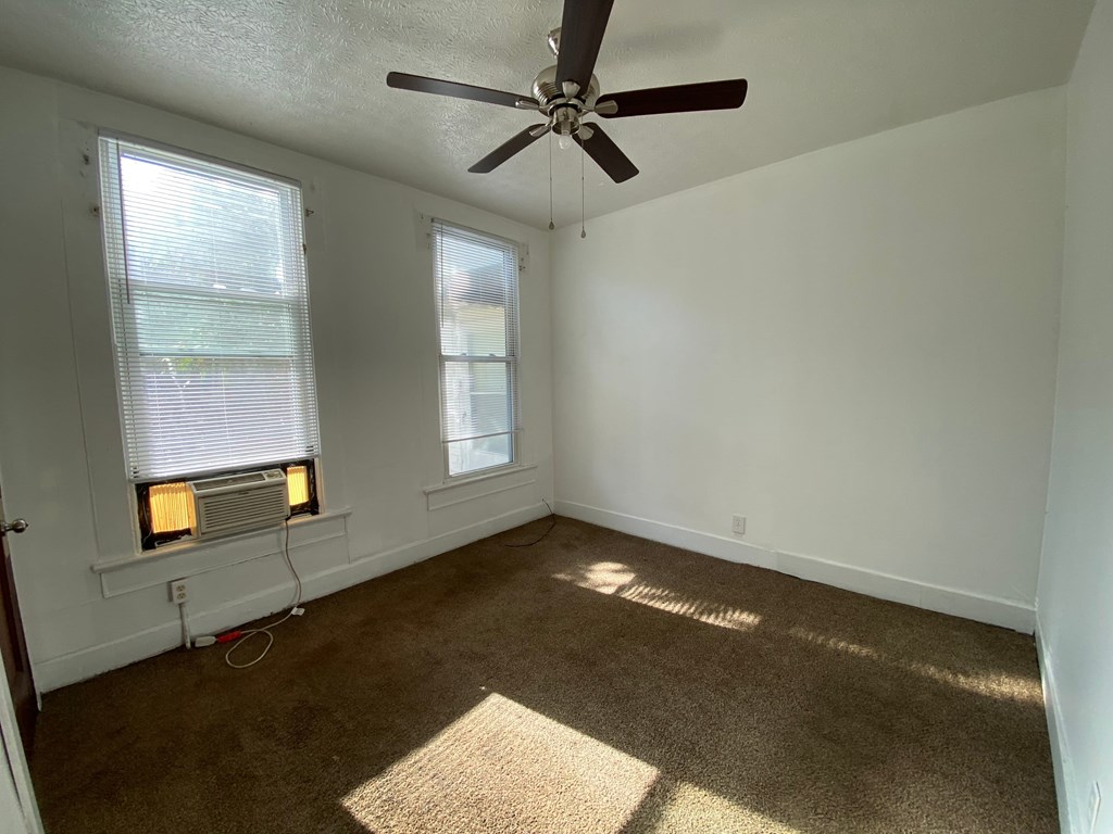 A room with a ceiling fan and two windows.