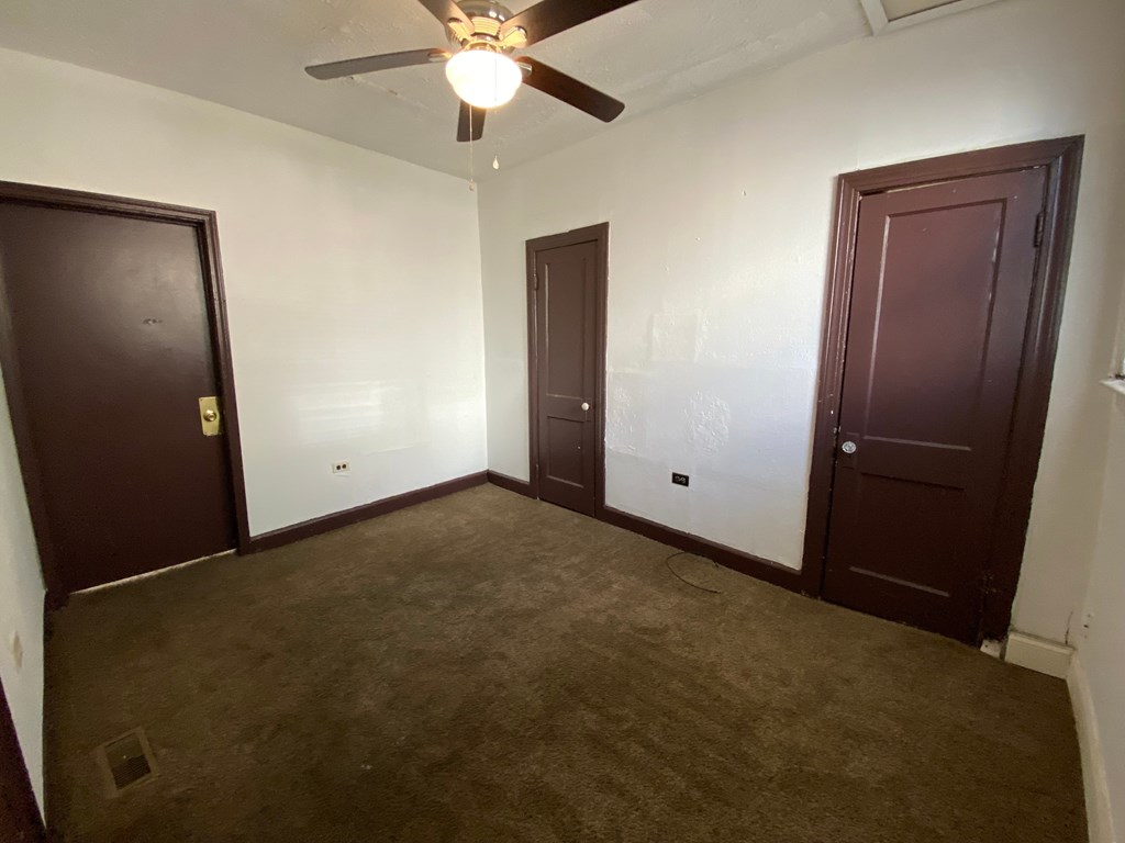 A room with a ceiling fan and three doors.