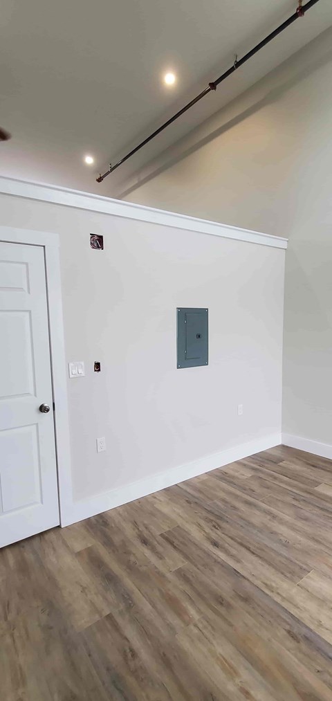 A room with a white door and a white wall with a brown wooden floor.
