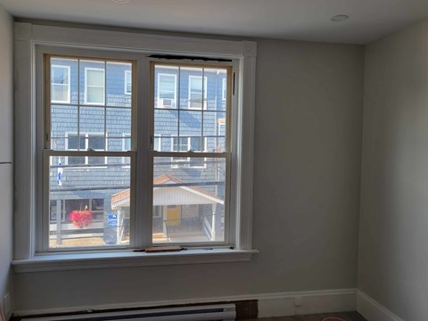 A window with a view of a building and a red flower.