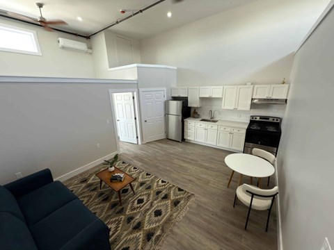 A living room with a couch, a coffee table, and a dining area with a refrigerator, oven, and sink.