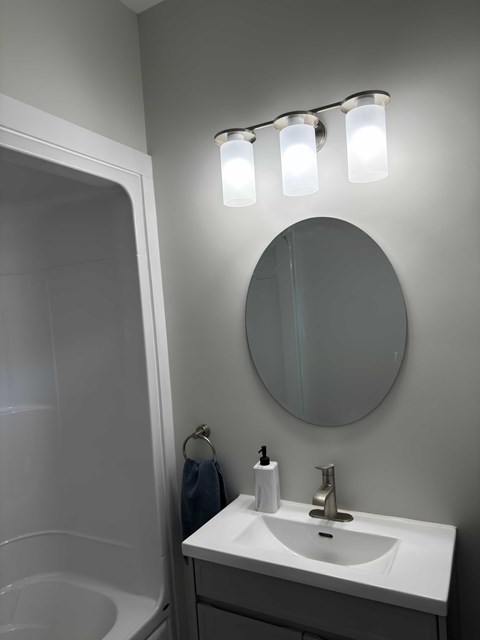 A bathroom with a white sink and a round mirror.