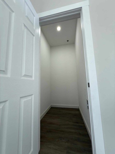 A white door is open to a small room with wood flooring.