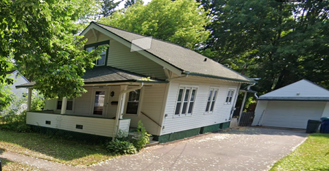 A house with a green roof and white walls is surrounded by trees.