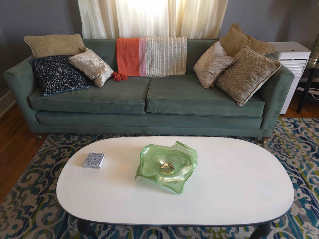 A green couch with pillows and a white coffee table in front of it.